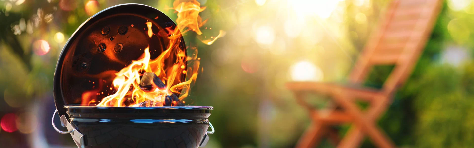 Kettle-style BBQ grill with flames, set in a sunny backyard, ready for outdoor cooking.